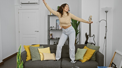 A joyful young woman dancing on a couch in a cozy apartment living room with modern decor.