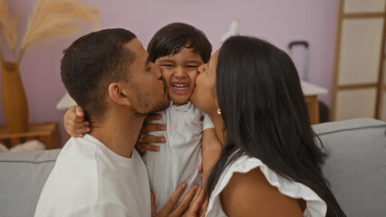 Fototapeta premium Latino family showing love as man and woman kiss their smiling child indoors in a cozy living room