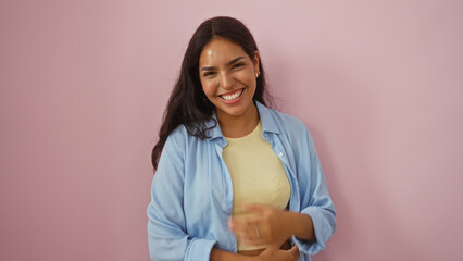 Young, attractive, hispanic woman smiling brightly against an isolated, pink background, exuding...