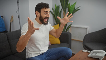 Excited middle-aged man with a beard gesturing in a modern living room with plants and a guitar.