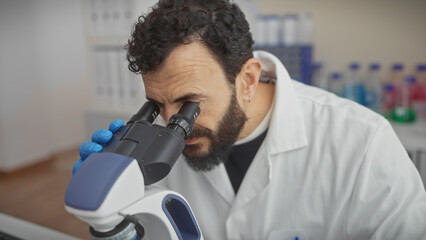 A middle-aged bearded man in a lab coat examines samples through a microscope in a laboratory setting.