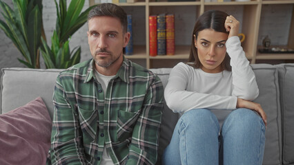 Obraz premium A thoughtful man and upset woman sitting together on a sofa in a modern living room looking distant.