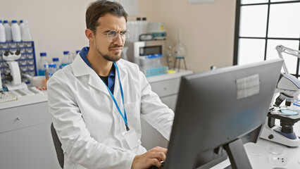 Hispanic man in lab analyzing data on computer indoors at hospital