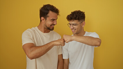 Father and son bonding with fist bump in front of an isolated yellow background, showcasing love and connection between two hispanic men.