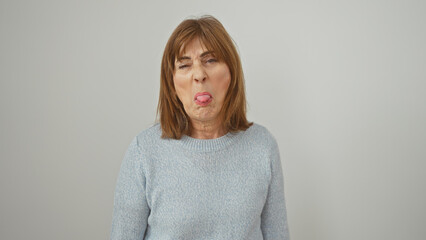 A middle-aged woman in a blue sweater sticking her tongue out against an isolated white background.