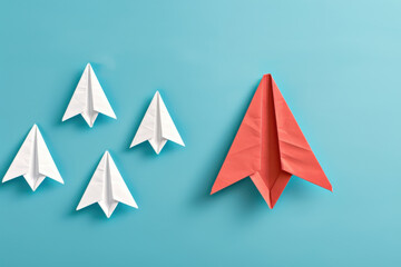 A red paper airplane standing out against a blue sky, followed by four white paper airplanes, symbolizing leadership.