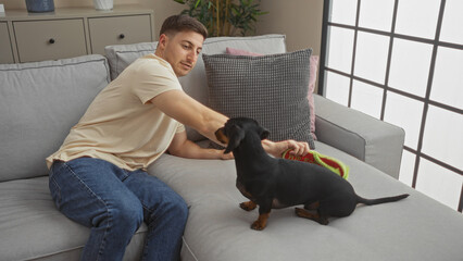 Hispanic man relaxing in a living room with a dachshund teckel dog while sitting on the sofa in an indoor home setting.
