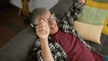 Obraz premium A cheerful senior man relaxing at home on a couch with bright pillows, embodying comfort and casual lifestyle.