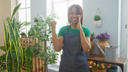 Smiling african american woman pointing sideways in an indoor flower shop with green apron and plants