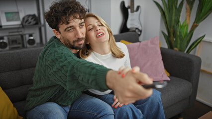 A loving couple enjoying leisure time in their cozy living room, the man holding a remote and the woman smiling in an embrace.