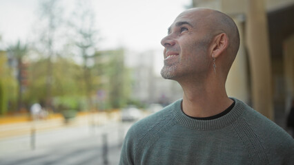 Smiling bald man with beard enjoying urban scenery outside on a sunny day.