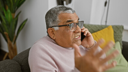 A senior man engages in a conversation on his mobile phone while relaxing on a couch in a cozy living room.