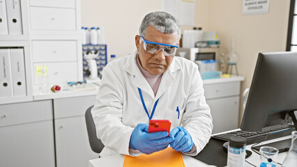 Middle-aged man in lab coat using smartphone in modern laboratory setting, embodying professionalism and concentration.