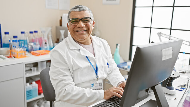 Smiling senior man scientist in lab coat working at computer in laboratory