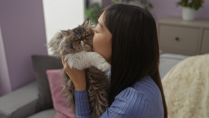 A young chinese woman affectionately holds and kisses her cat in the comfortable living room of her home, highlighting pet companionship and domestic tranquility.