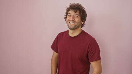 A cheerful young hispanic man with a beard smiling against a soft pink isolated background.