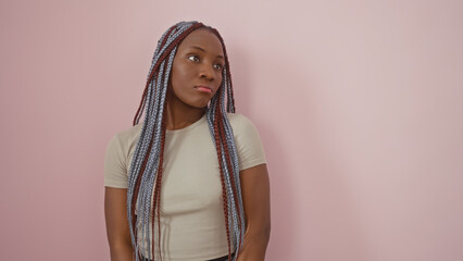 African american woman with braids posing against a pink isolated background portrays thoughtfulness and beauty.