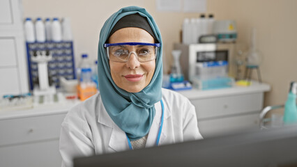 Smiling woman scientist wearing hijab and safety glasses in laboratory setting, exuding professionalism and knowledge.