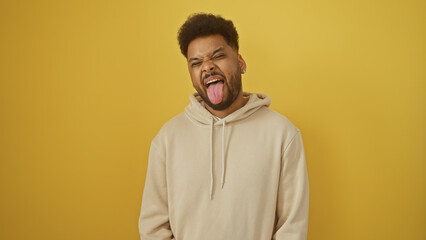 Handsome black man making a funny face against a yellow background while wearing a casual hoodie.