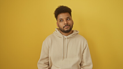 Portrait of a thoughtful african american man in casual beige hoodie against a vibrant yellow background.