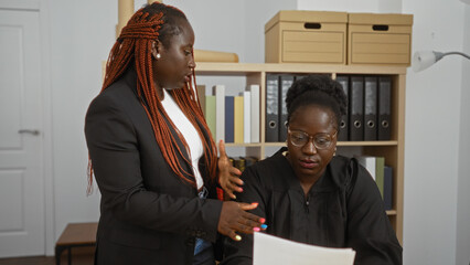 African american women, one a lawyer and the other a judge, discussing documents in an office setting.
