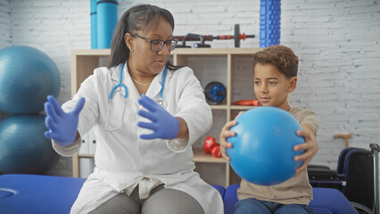 Therapist woman, boy patient playing ball during physiotherapy in a clinic.