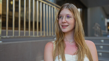 Young, attractive, blonde, woman smiling on a city street, exterior scene, with urban background