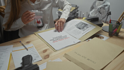 Caucasian woman detective examines evidence at a police department's office, surrounded by documents.