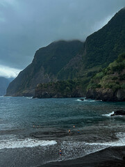 Seixal Beach with black sand and green mountains with clouds. Seixal, Madeira, Portugal