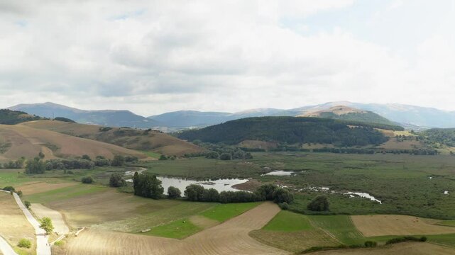 Aerial view of the wild Colfiorito Plateau in Central Italy, nestled in the Apennines between Umbria and Marche. The landscape is mostly untouched, with farmland and a few small roads