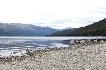 A tranquil lakeshore with mountains in the background under a cloudy sky