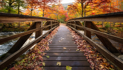 Fototapeta premium A rustic wooden bridge over a forest stream, adorned with fallen leaves and surrounded by the rich golds and reds of autumn trees.