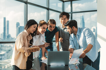 Asian project manager uses laptop displayed data analysis while professional business team brainstorming marketing idea at business meeting. Working together,sharing idea, planing strategy. Tracery.