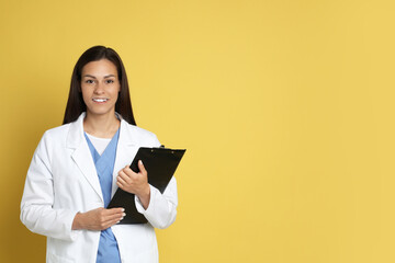 Fototapeta premium Portrait of smiling nurse with clipboard on yellow background. Space for text