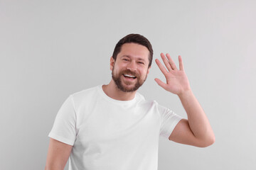 Fototapeta premium Cheerful handsome man waving on light background