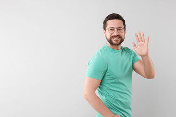 Cheerful man waving on light background. Space for text