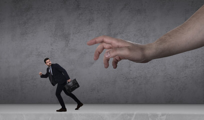 Big hand catching running away small businessman on grey background. Authority, abuse, conflict...
