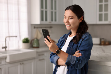 Smiling woman using smartphone in kitchen. Space for text