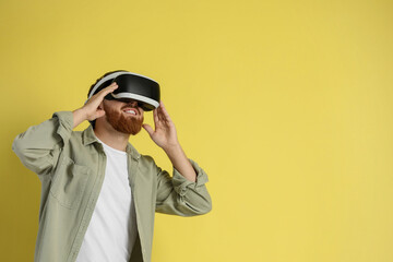 Happy man using virtual reality headset on pale yellow background. Space for text