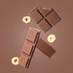 Pieces of tasty chocolate and hazelnuts in air on pale brown background