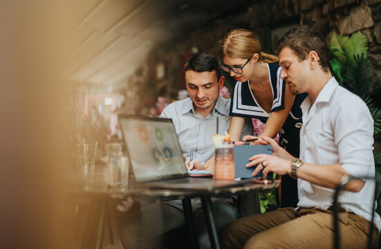 A group of young professionals in a modern cafe, working together on a laptop and tablet, sharing ideas and collaborating on a project.