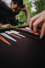 A person playing backgammon outdoors, focusing on the game board. Captures leisure, relaxation, and strategy in a natural setting.