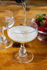 Pouring of brut champagne bubbles wine in coupe glasses and small bowl with fresh strawberries