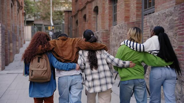 Rear view of multiracial group cheerful erasmus students walking hugging enjoying free time outdoor. Young friends embracing together strolling university campus. Gen z colleagues, youth relationships