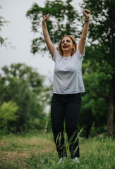 A joyful woman raises her arms in celebration while enjoying nature in a lush green park.