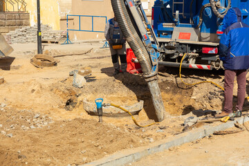 Workers use a suction excavator based on a truck to sample soil in a well for communications