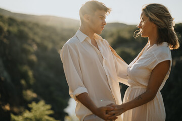 Obraz premium Young couple in love holding hands and sharing a romantic moment in nature at sunset. Warm and tender emotions in a scenic outdoor setting.