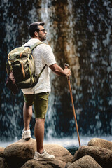 Man with backpack and hiking stick looking at waterfall