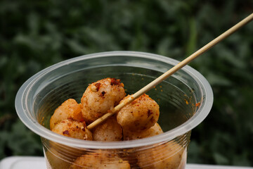 Close-up of Cipak Koceak, a popular Indonesian street food snack, seasoned with spicy chili powder, served in a plastic cup with a skewer for easy eating