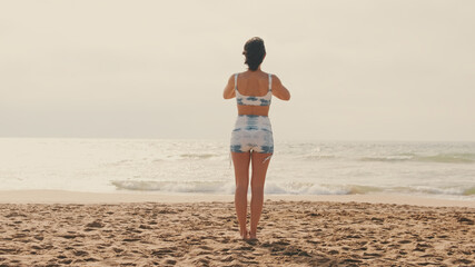 Close-up back view of a girl doing yoga on the beach, yoga class by the sea, graceful female athlete